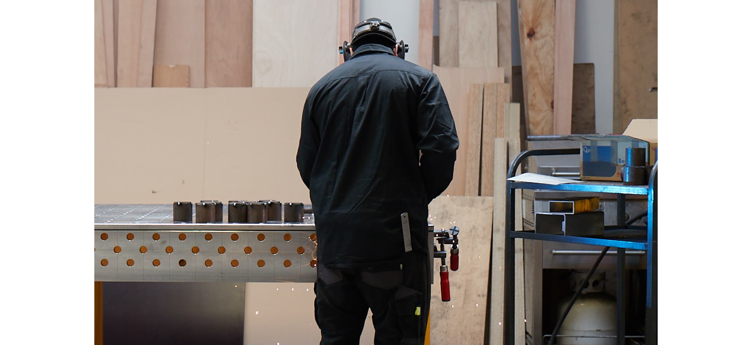 A metal worker at a bench in a workshop with their back to the camera.